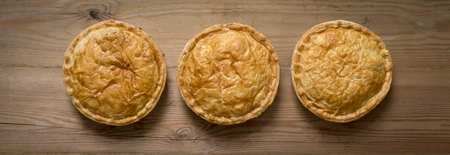 Overhead view of three cooked round meat pies on a wooden countertopの写真素材