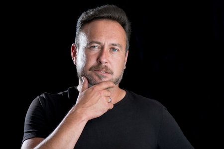 Man with thumb and finger on his chin as if thinking over a black background