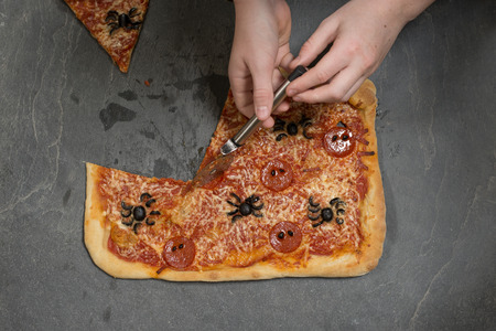 Hand slicing a halloween-themed pizza using a pizza cutterの写真素材