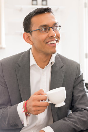 Guy in business attire holding a tea cup smiling while looking away.