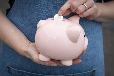 Female hands inserting coin into a pink piggy bankの写真素材