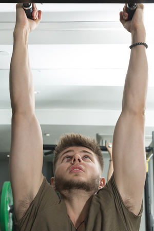 Young man grabbing on to pull-up bar in a gymの写真素材