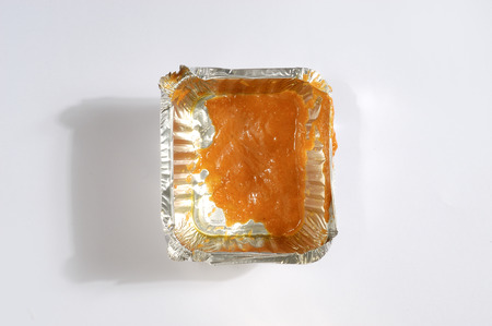 Overhead of a used aluminum foil tray with leftover orange sauce on white backgroundの写真素材