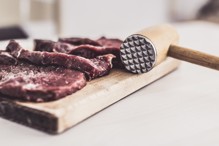Uncooked seasoned beef slices and a meat hammer on a wooden cutting boardの写真素材