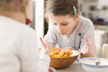 Little girl looks at a bowl of french fries in excitementの写真素材
