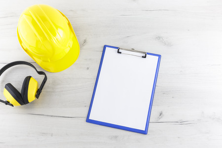 Hard hat, earmuffs, and a clipboard on a white wooden surfaceの写真素材