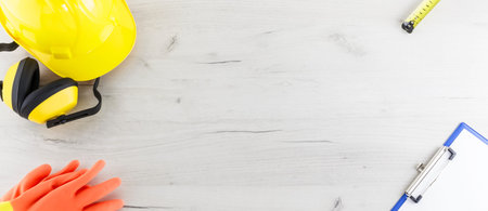 Banner image of hard hat, earmuffs, gloves, tape measure, and a clipboard flat lay on a white wooden...