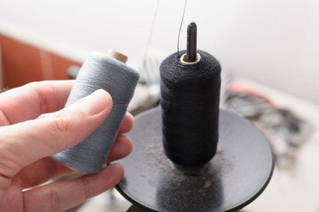 Spool of gray thread in hand and spool of black thread in a sewing machine pin