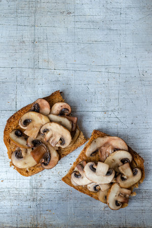 Mushrooms on toast servings on worn stainless steel background overhead view with copy spaceの写真素材