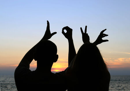 A silhouette of a romantic couple holding their hands spelling the word \"LOVE\" on the background of a sea sunset.の写真素材