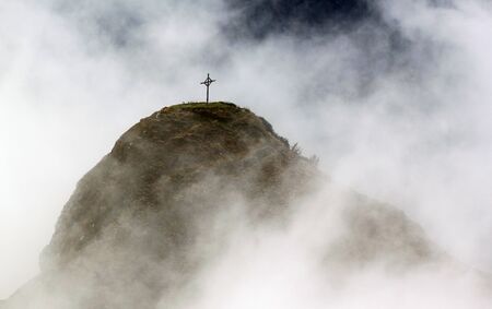 A single cross stands on a moutnain engulfed in white clouds.の写真素材