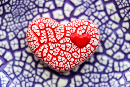 Red speckled clay heart on purple speckled background.の写真素材