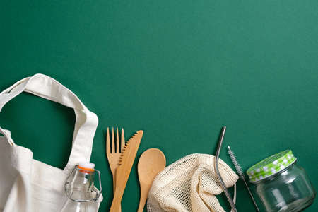 Eco friendly bamboo cutlery, glass jar, bottle, reusable canvas shopper bag and metal drinking straws on green background. Zero waste, plastic free concept. Sustainable lifestyle. Flat lay, top view.の写真素材