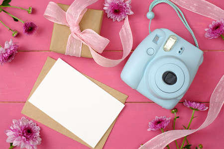 Female desk with blank paper card, gift box, instant photo camera and daisy flowers on pastel pink background. Feminine accessories on the wooden table. Creative layout, beauty blogger desk conceptの写真素材
