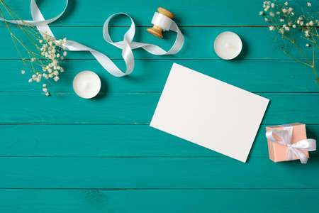 Blank wedding invitation card on stylish woman's desk on green wooden background. Flat lay composition, top view, overhead. Anniversary celebration concept.の写真素材