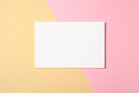 Blank white paper card on two color pastel pink and yellow background. Flat lay, top view, overhead....
