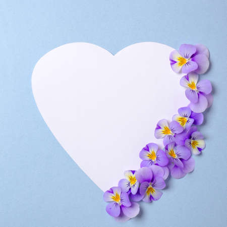 Floral frame border made of white heart-shaped paper, flowers petals, green leaves on watercolor spring background. Invitation, greeting card or an element for your design. Top view, abstract art.の写真素材