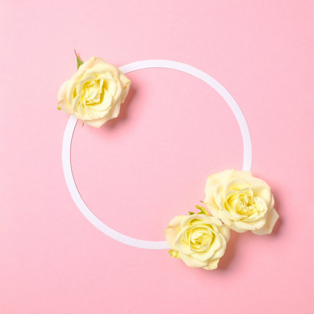 Round floral frame with roses flowers petals on pastel pink background. Top view, tender minimal...