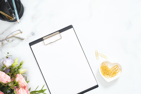 Modern home office desk workspace with blank paper clipboard, roses flowers bouquet, glasses, golden...