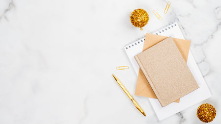 Christmas office desk table concept. Feminine workspace with golden Xmas balls, pen, paper notepad and notebook on marble background. Flat lay, top view, copy spaceの写真素材