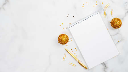 Christmas home office desk table concept. White marble background with blank paper notepad and Xmas tree, golden balls decor, pen, confetti. Flat lay minimal style composition, top view, copy space.の写真素材