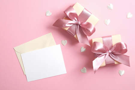 Romantic love letter with white paper note mockup and two gift boxes with ribbon bow on pink background decorated Valentine's hearts. Minimal flat lay style composition, top view.の写真素材