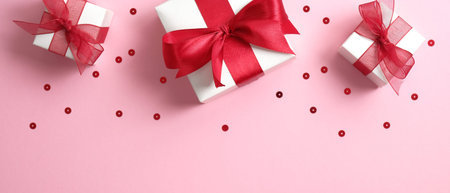 Valentine's Day banner with white gift boxes decorated red ribbon bow on pink background with confetti. Flat lay, top view.の写真素材