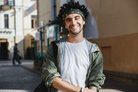 Smiling handsome man, happy hipster guy with dreadlocks hairstyle posing outdoor in the city street. Rastafarian lifestyle. Close up portrait of man dressed autumn fashion stylish outfit enjoying lifeの写真素材