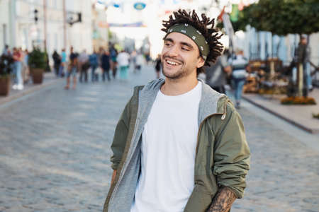 Young handsome beard man dressed stylish casual clothes, white t-shirt, green jacket, bandana posing outdoor. Smiling hipster with dreadlocks hairstyle, close up portrait, street photo, urban styleの写真素材
