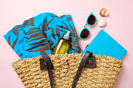 Summer beach bag with elegant women's accessories on pink background. Top view beach bag with dress,...