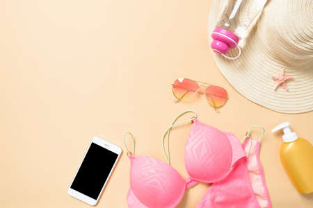 Vacation, travel, tourism, technology and accessories concept - close up of smartphone and beach women's stuff: swimwear, sunglasses, suntan, straw hat on yellow background. Flat lay, top view.の写真素材