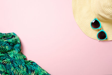 Straw hat, sunglasses, scarf on pastel pink background with copy space for text. Summer female...