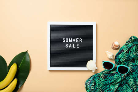 Women's beach accessories: straw hat, sunglasses, green scarf, banana and letter board with sign "SUMMER SALE" on yellow background. Summer sale banner template concept. Flat lay composition, top viewの写真素材