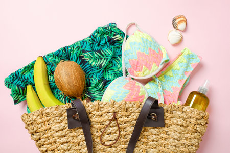 Summer beach bag with elegant women's accessories and fruits on pastel pink background. Top view on...