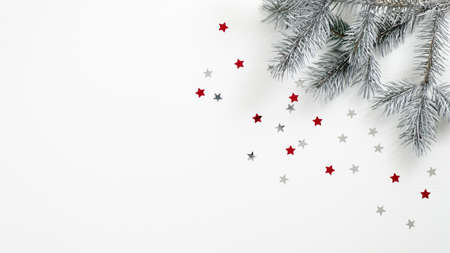 Christmas tree branch and confetti stars on white background. Flat lay, top view, copy space. Xmas banner mockup, winter holidays frame, greeting card templateの写真素材