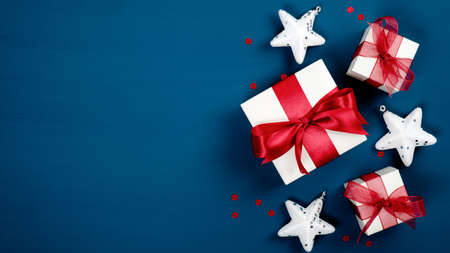Christmas gifts with red bows and star decorations on dark blue background. Flat lay, top view. Christmas, winter holidays, New Year concept. Xmas banner mockup.の写真素材