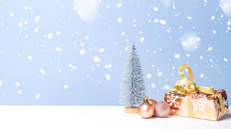 Small Christmas tree with present and balls in snow on blue background. Christmas banner with copy space, New Year greeting card.の写真素材