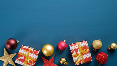 Christmas frame border with red and golden decorations on blue background. Top view wooden...