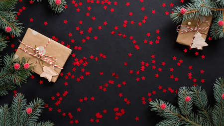 Christmas banner mockup. Flat lay red confetti, gift boxes and fir tree branch on black background. Top view.の写真素材