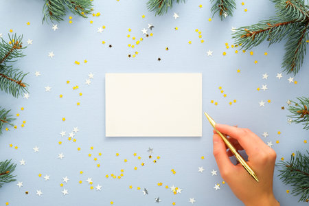 Top view of woman hands writing on a blank paper greeting or invitation card over blue background...