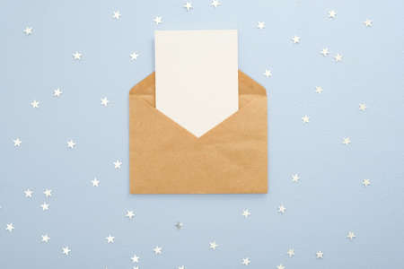Empty blank card in kraft paper envelope on pastel blue background decorated with confetti star. Christmas, New Year, winter holiday invitation mockup.の写真素材