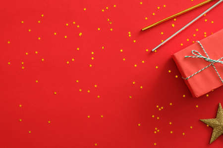 Christmas party background. Invitation card mockup. Red gift box, golden star and confetti, drinking straw on red background. Flat lay, top view, copy space. Christmas party poster templateの写真素材
