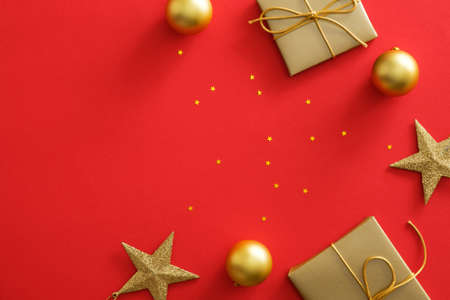 Christmas gold decorations on red background with copy space. Flat lay golden gift box, baubles, stars, glittering confetti. Christmas poster mockup, greeting card template, website header heroの写真素材