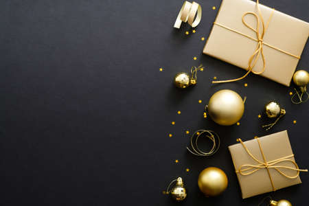 Elegant Christmas background with modern golden Christmas decorations, baubles, gift boxes, confetti stars on dark black backdrop. Flat lay design, top view, copy space.の写真素材
