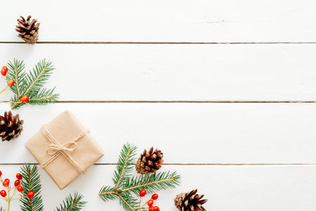 Christmas composition. Christmas frame made of fir tree branches, red berry, gift boxes, cones on wooden white background. Flat lay, top view, copy space. Christmas, New Year, winter holiday conceptの写真素材