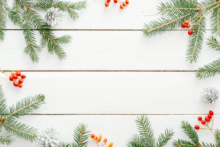Christmas composition. Christmas frame made of fir tree branches and red berry on wooden white background. Flat lay, top view, copy space. Christmas background, Xmas postcard template, banner mockupの写真素材