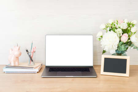 Home office desk table with laptop computer with blank white screen, supplies, picture frame, feminine accessories and flowers bouquet on wooden surface. Stylish woman workplace concept.の写真素材