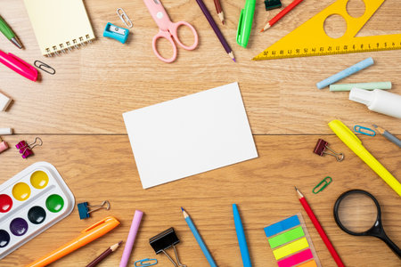 School supplies on wooden table, background with frame made of stationery and blank paper card in...