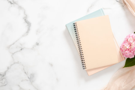 Blank paper notebook, pink hydrangea flower, pastel blanket on marble background. Flat lay, top view...