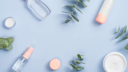 Natural organic beauty product concept. Frame of organic cosmetic products on blue background with copy space. op view essential oil, lotion, cream jar and eucalyptus leaves.の写真素材